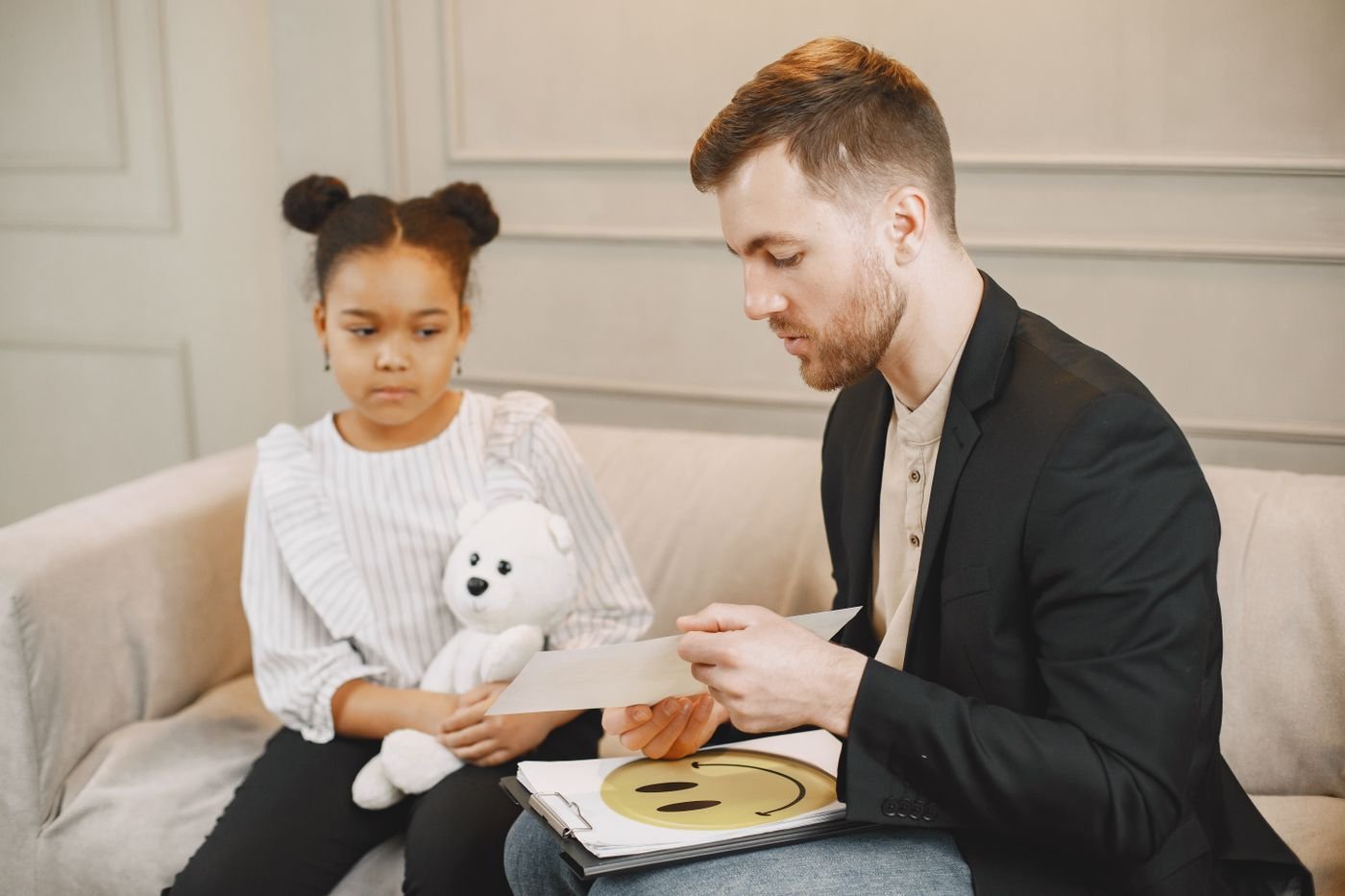 A therapist talking with a young girl holding a plush toy